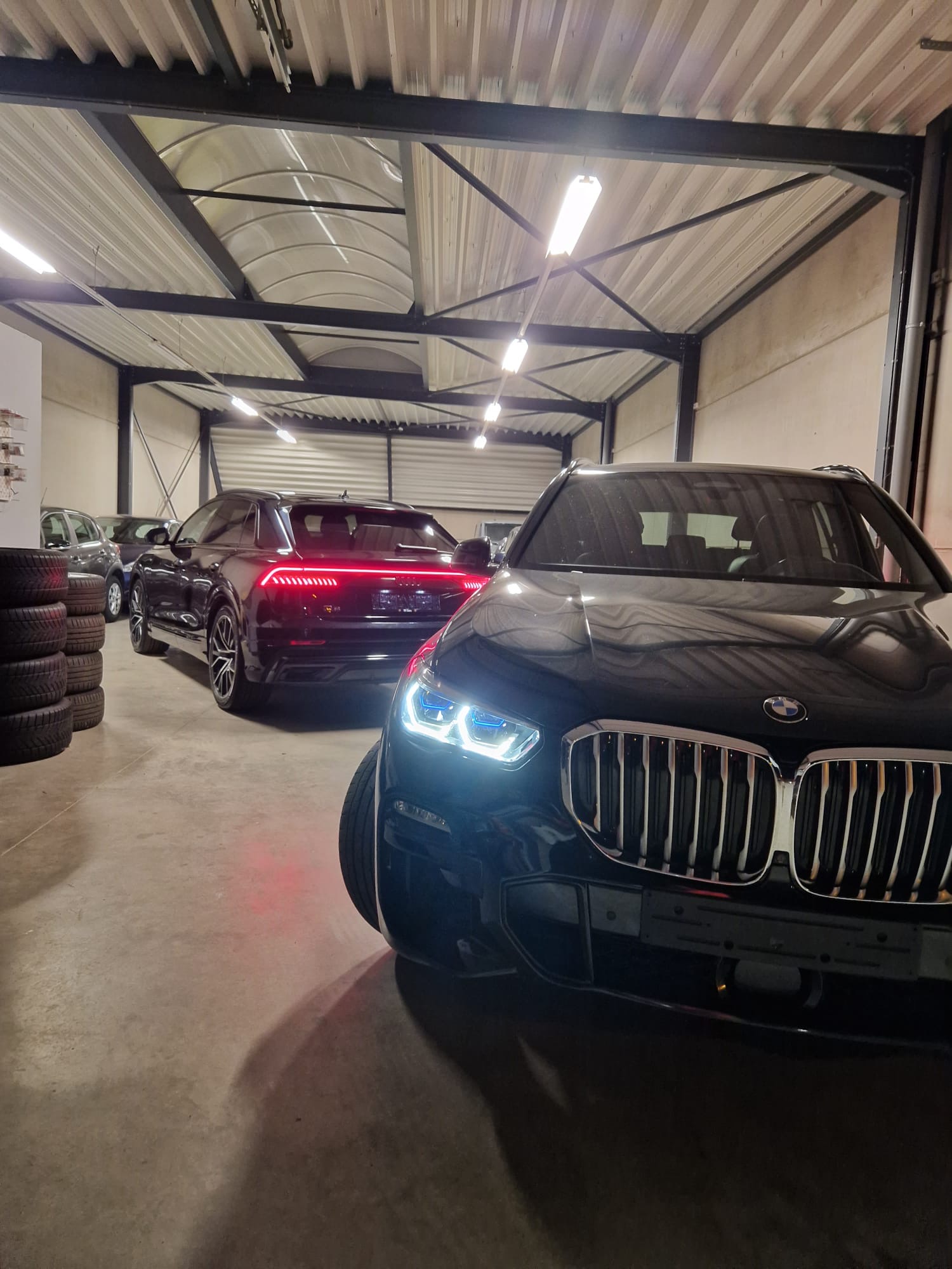 BMW X6 and Audi Q8 inside the R1 Cars garage with evening lights